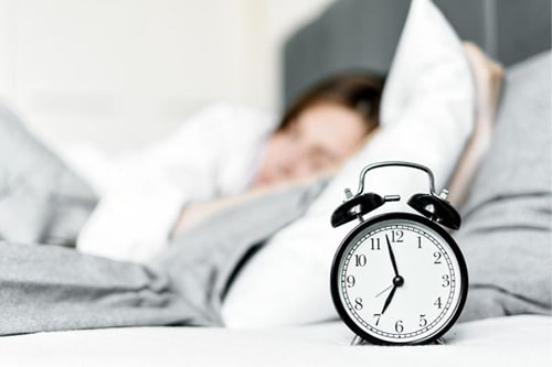 Alarm clock by bed with white sheets